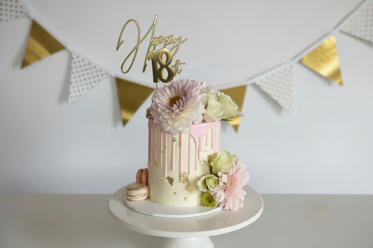 Small cake with flowers and a 'Happy 18th' topper on a white background